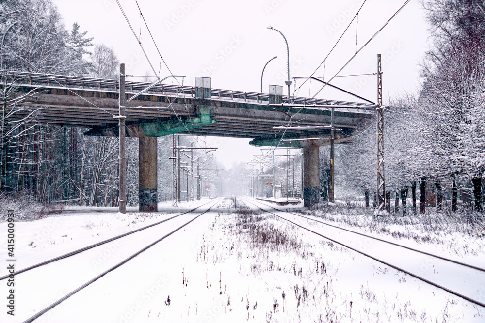 Snow-covered two track tracks for the train and a car viaduct across them.