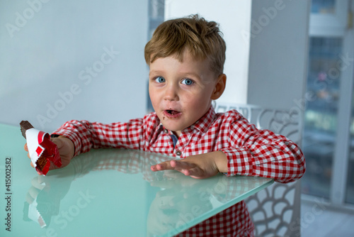 Valokuva Boy eats a chocolate bar while sitting in kitchen.