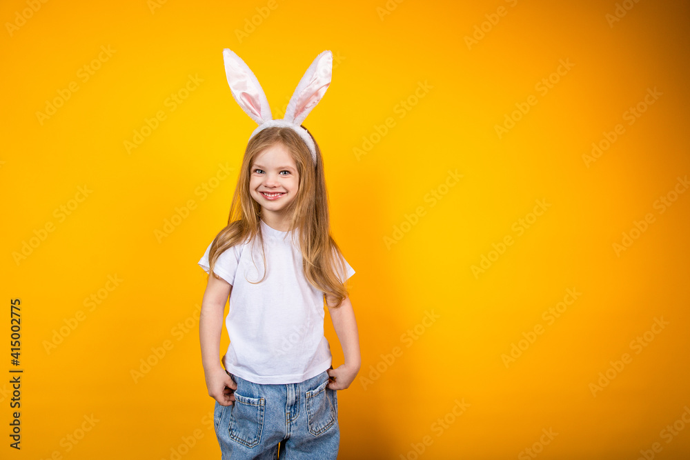 Baby girl in white T shirt wearing bunny ears posing on yellow background