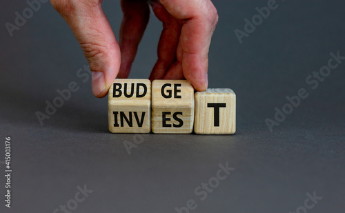 Invest or budget symbol. Businessman turne wooden cubes and changes the word 'invest' to 'budget'. Beautiful grey background, copy space. Business, invest or budget concept. photo