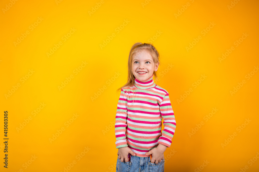 Funny little girl in a striped sweatshirt standing on a yellow background with markers in the pockets of her jeans