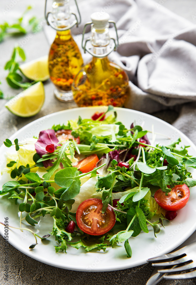 Fresh green mixed salad bowl with tomatoes and microgreens on concrete background. Healthy food, top view. Fresh green mixed salad bowl with tomatoes and microgreens on concrete background. Healthy food, top view.