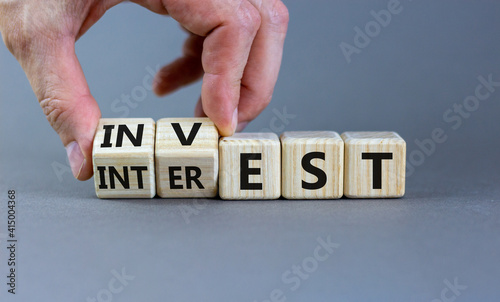 Invest or interest symbol. Businessman turns wooden cubes and changes the word 'invest' to 'interest'. Beautiful grey background, copy space. Business and invest or interest concept.