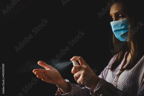 Happy girl medical face mask apply antiseptic gel on hand isolated on black background. Beautiful stylish hipster woman in protective face mask using antibacterial sanitizer. Hygiene, safety