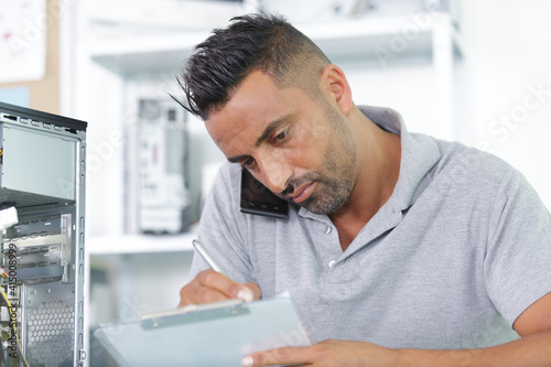 man holding mobile phone between ear while writing notes