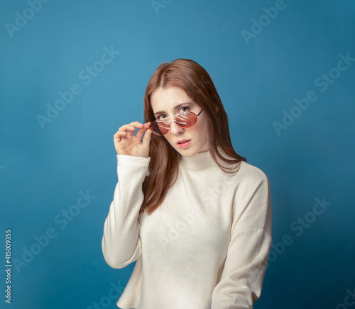 redhead woman looking over her glasses in a blue background