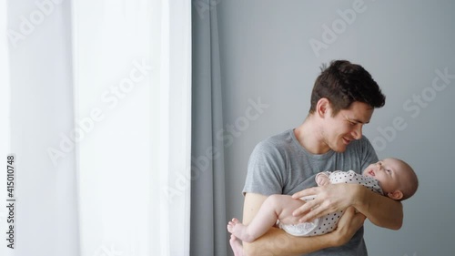 Young happy father holds a newborn baby in his arms. Kisses, smiles