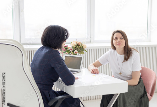 two young women conduct a coaching session in home office in light interior with laptop and flowers on tablework with metaphorical cards and psychological counseling photo