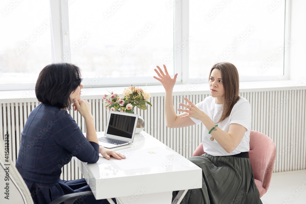 two young women conduct a coaching session in home office in light interior with laptop and flowers on tablework with metaphorical cards and psychological counseling two young women conduct a coaching session in home office in light interior with laptop and flowers on tablework with metaphorical cards and psychological counseling