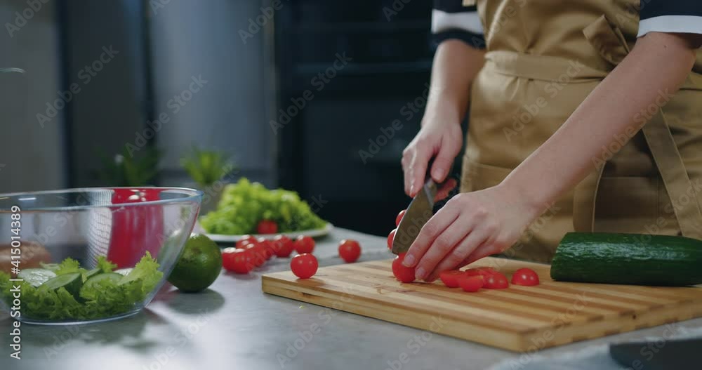 Unknown woman holding a knife in her hands and cutting tomatoes while cooking vegetable salad near kitchen table ,close up Unknown woman holding a knife in her hands and cutting tomatoes while cooking vegetable salad near kitchen table ,close up
