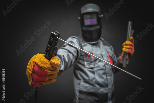 Tableau sur toile A welder in a helmet with a welding terminals in hand on a black background