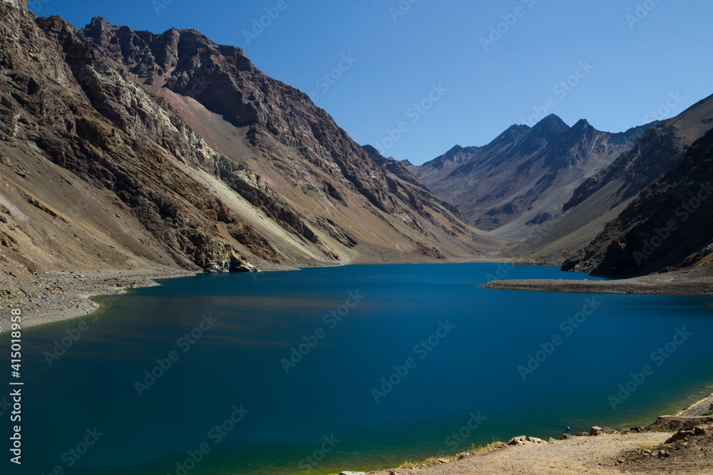 The deep blue color water lake very high in the Andes mountains. View of the Inca Lagoon in Chile,  surrounded by rocky mountains and cliffs. 