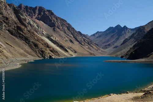 The deep blue color water lake very high in the Andes mountains. View of the Inca Lagoon in Chile, surrounded by rocky mountains and cliffs. 