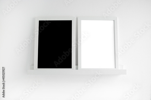 Two white frames with a black background and a white background on a white shelf in a light interior. Abstract minimalistic background