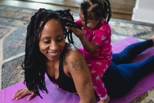 Smiling mid-30s mother and happy toddler at home on yoga mat, exercising and playing photo