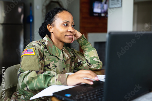 Happy military woman listening to family while working from home at laptop