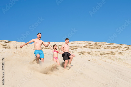 Children with their father run along the beach sand. Family on vacation, leisure, sports, lifestyle