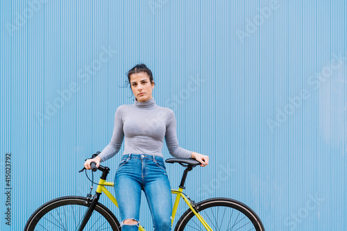 Confident mid adult woman sitting on fixie bike against blue wall photo