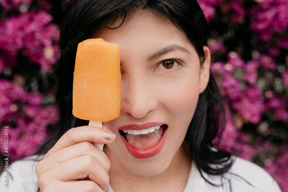 Happy woman with mouth open covering eye with orange ice cream Happy woman with mouth open covering eye with orange ice cream
