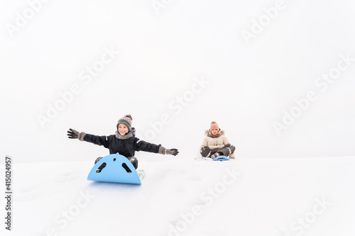 Playful sister and brother sledding on snow covered hill