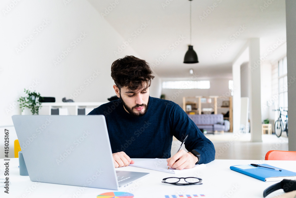 Young businessman writing at desk in creative office Young businessman writing at desk in creative office