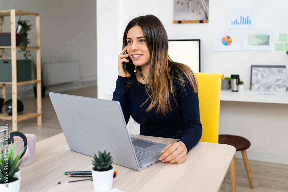 Smiling female freelancer on phone call while sitting by laptop at home Smiling female freelancer on phone call while sitting by laptop at home