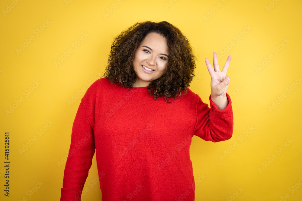 Young african american woman wearing red sweater over yellow background showing and pointing up with fingers number three while smiling confident and happy Young african american woman wearing red sweater over yellow background showing and pointing up with fingers number three while smiling confident and happy
