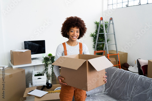 Smiling young holding cardboard box while standing in new home during relocation