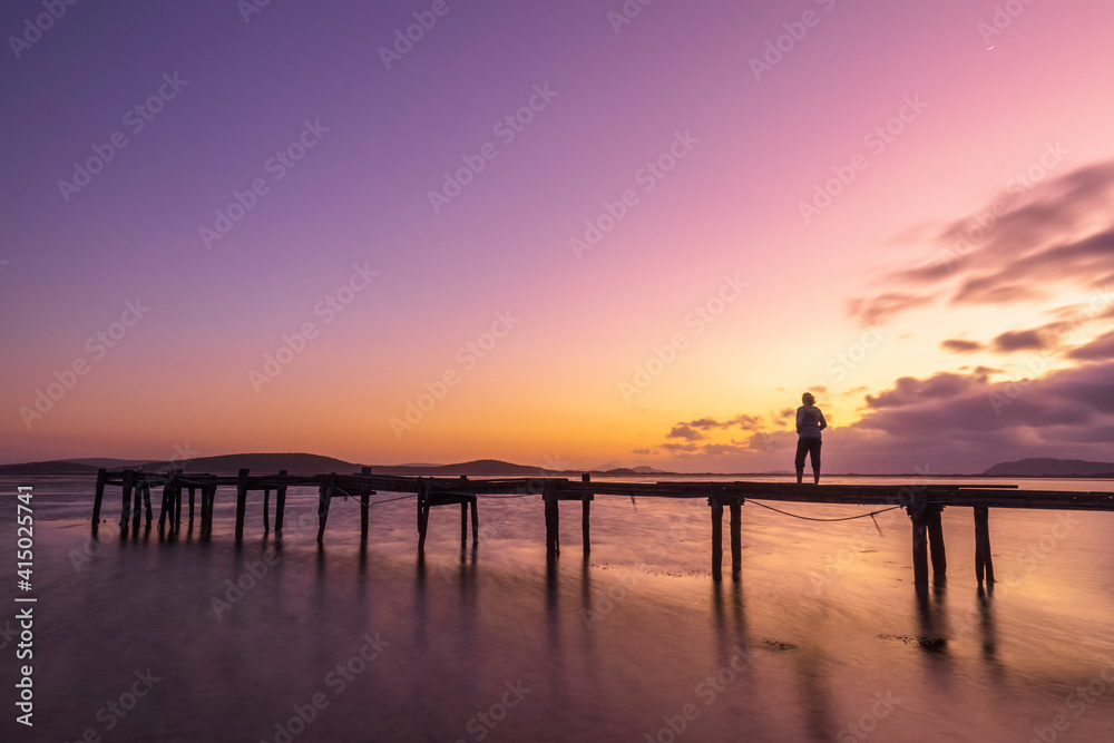 Silhouette of woman standing alone on coastal jetty at moody dawn Silhouette of woman standing alone on coastal jetty at moody dawn