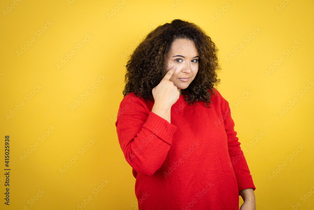 Young african american woman wearing red sweater over yellow background Pointing to the eye watching you gesture, suspicious expression Young african american woman wearing red sweater over yellow background Pointing to the eye watching you gesture, suspicious expression