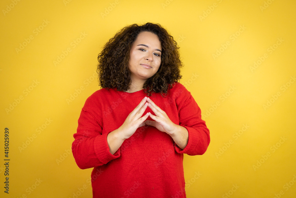 Young african american woman wearing red sweater over yellow background with Hands together and fingers crossed smiling relaxed and cheerful. Success and optimistic Young african american woman wearing red sweater over yellow background with Hands together and fingers crossed smiling relaxed and cheerful. Success and optimistic