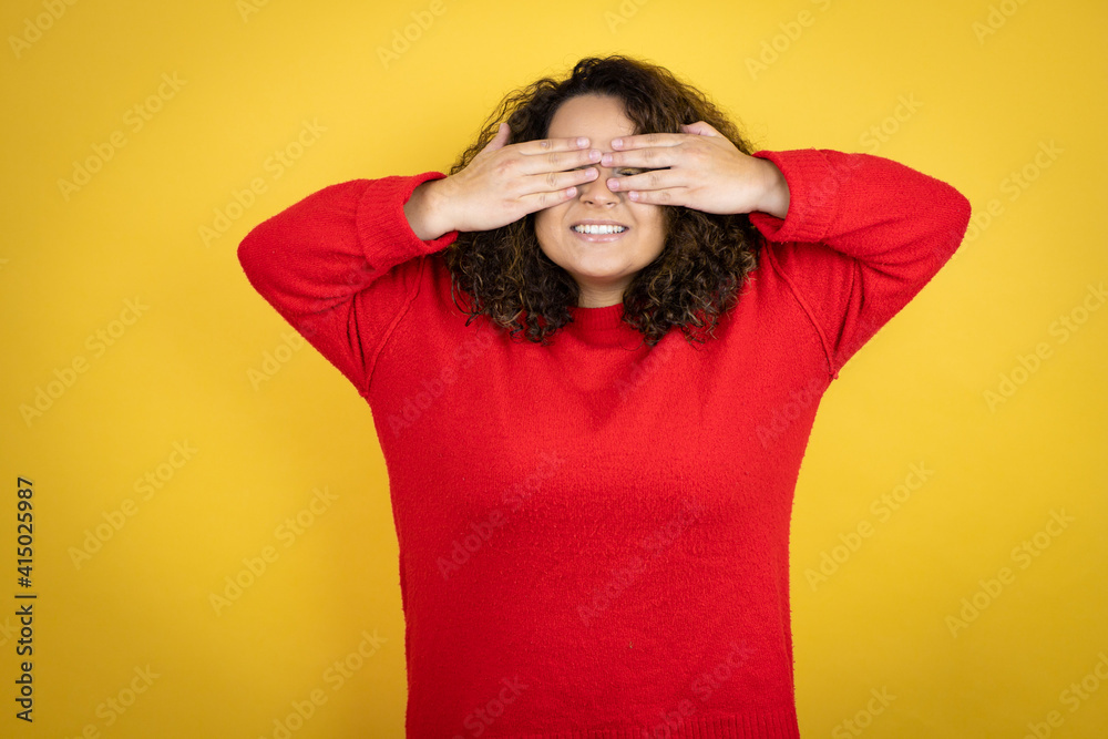 Young african american woman wearing red sweater over yellow background covering eyes with hands smiling cheerful and funny. Blind concept. Young african american woman wearing red sweater over yellow background covering eyes with hands smiling cheerful and funny. Blind concept.