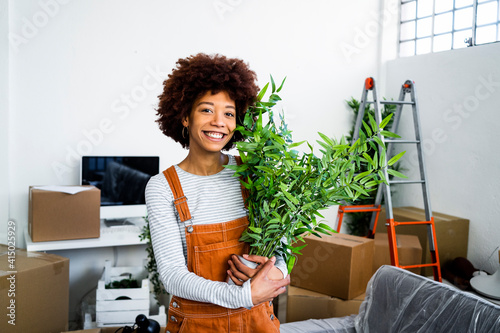 Happy afro woman holding potted plant during relocation in new apartment