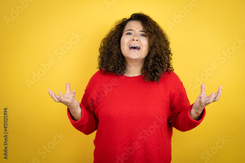 Young african american woman wearing red sweater over yellow background crazy and mad shouting and yelling with aggressive expression and arms raised. Frustration concept.