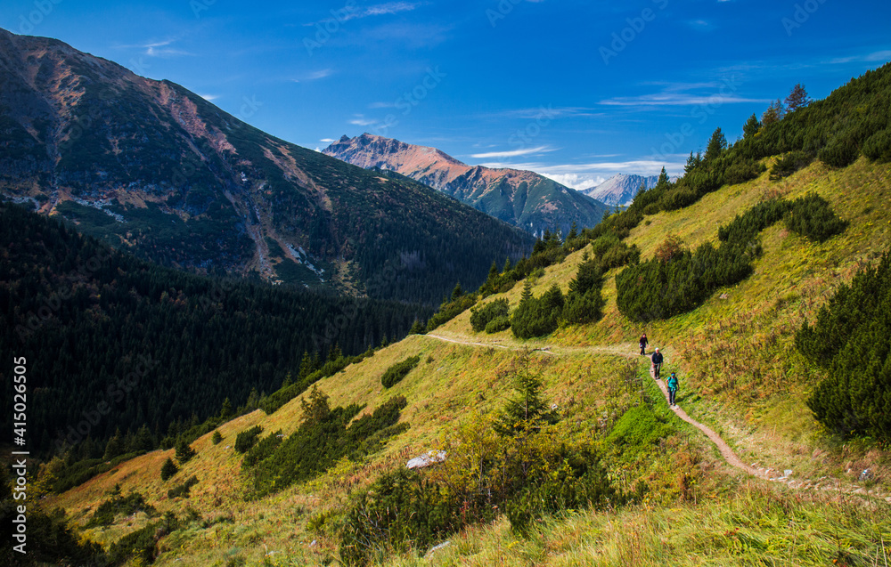 Hikers walking on hiking trail on a hillside above valley with mountains in the backgroud