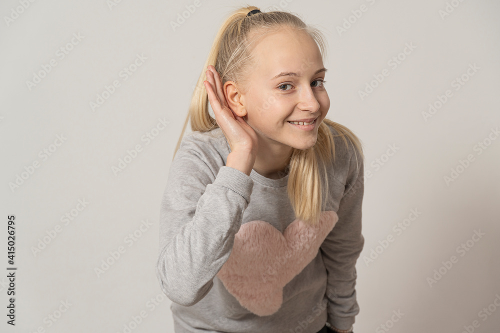 teenage girl smiling with her hand above her ear, listening to rumors or gossip. deafness concept. teenage girl smiling with her hand above her ear, listening to rumors or gossip. deafness concept.
