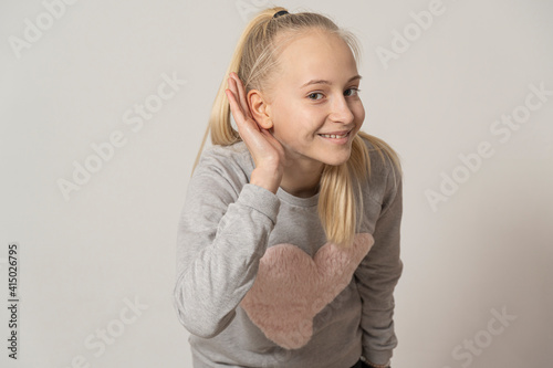 teenage girl smiling with her hand above her ear, listening to rumors or gossip. deafness concept.