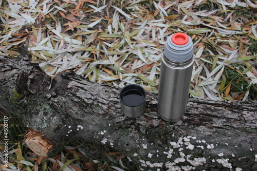 Camping thermos on the fallen log against the background of the fallen leaves. Hiking concept