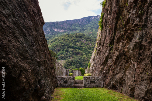 Grass lane amidst soapstone cliffs at quarry in Parco Archeologico Botanico del Paradiso, Valchiavenna, Chiavenna, Province of Sondrio, Lombardy, Italy