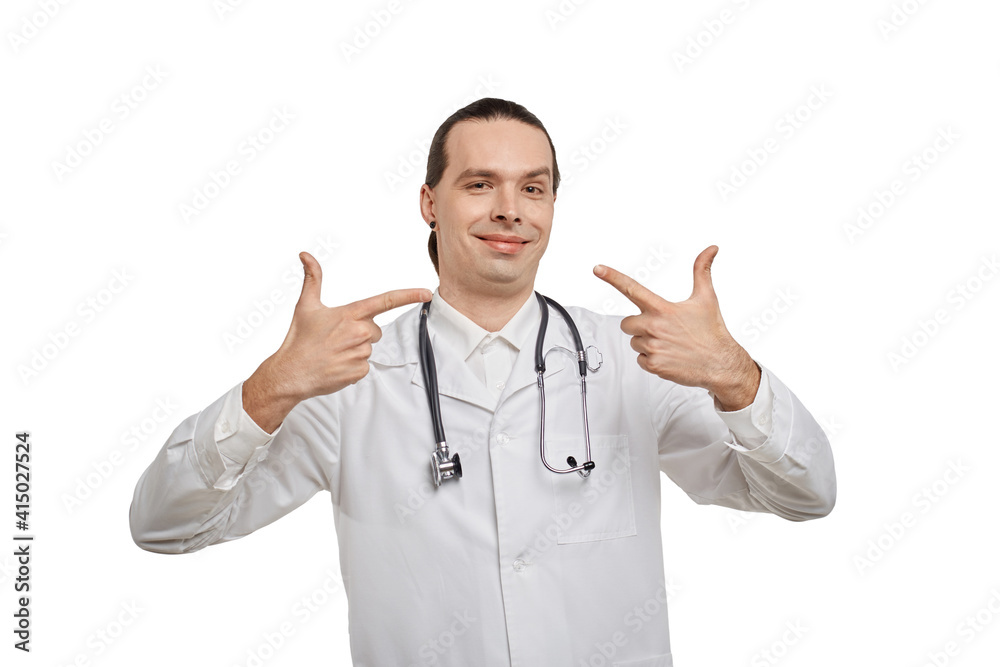 A male doctor in a medical gown smiles and points at the face. White isolated background. A male doctor in a medical gown smiles and points at the face. White isolated background.