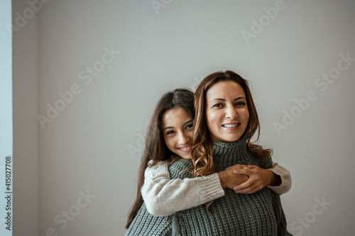 Happy daughter embracing mother while standing against white wall at home