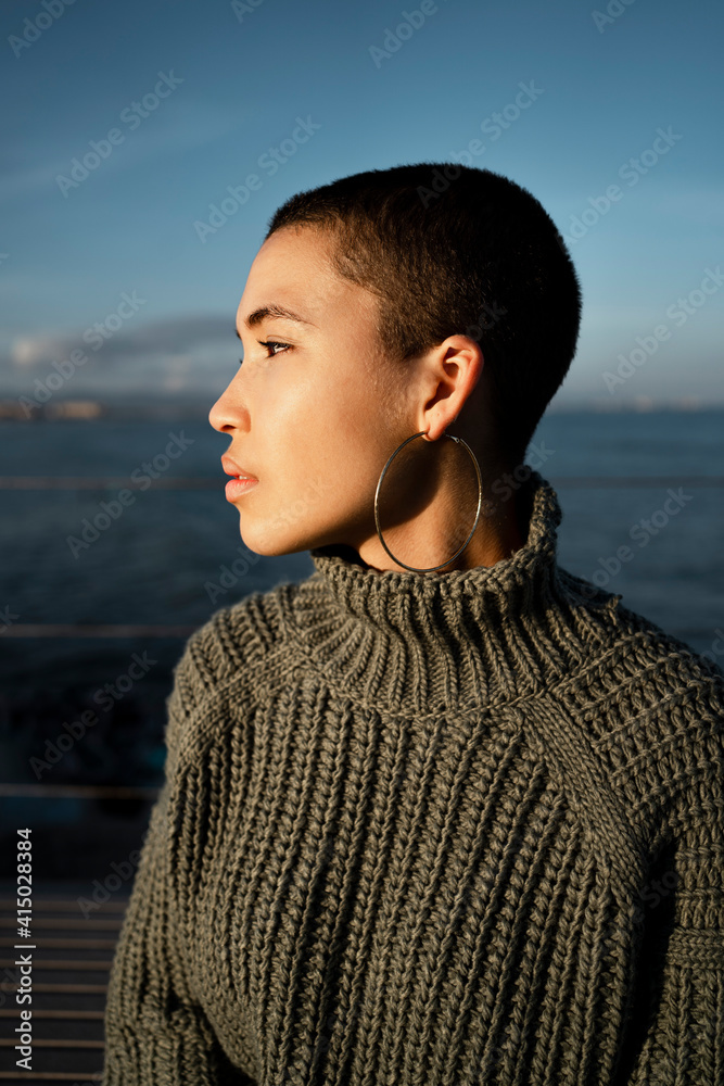 Young woman wearing turtleneck sweater looking away while sitting against sky Young woman wearing turtleneck sweater looking away while sitting against sky