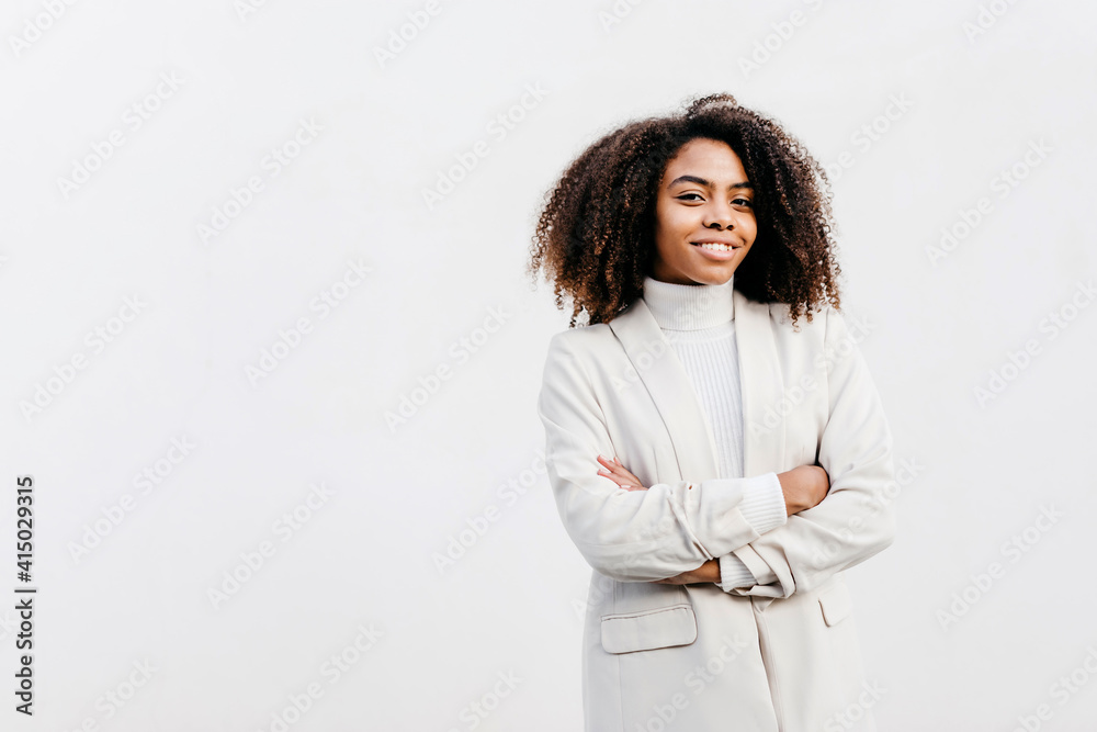 Smiling afro young woman with arms crossed standing against white wall Smiling afro young woman with arms crossed standing against white wall