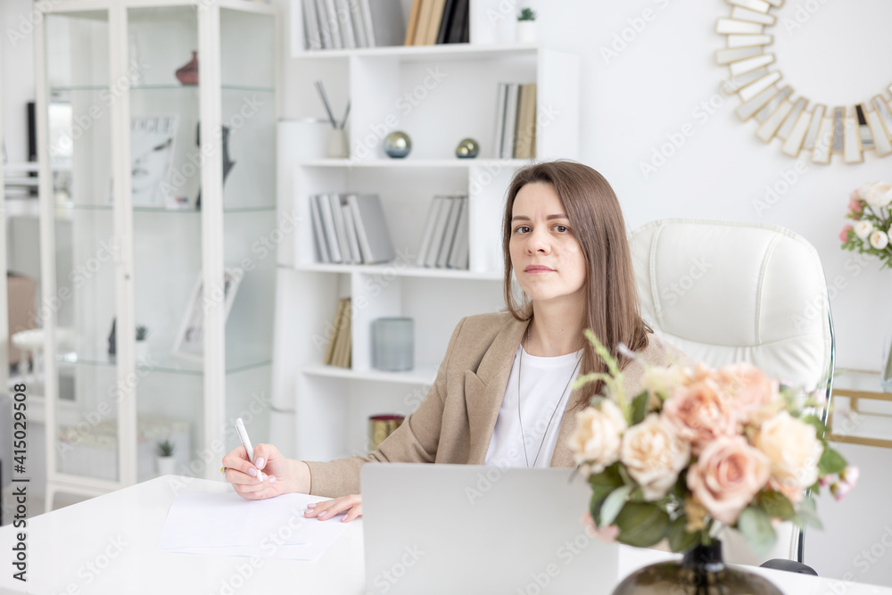 a young female coach works in a home office in a light interior with a laptop and flowers on the table, the concept of remote work a young female coach works in a home office in a light interior with a laptop and flowers on the table, the concept of remote work