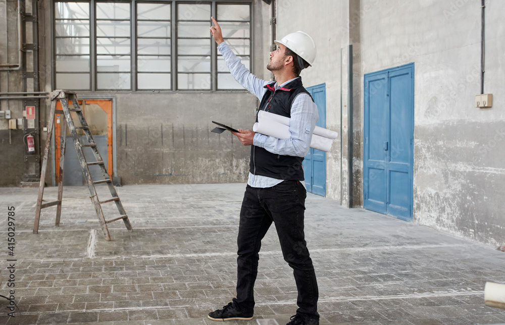 Male architect with digital tablet pointing while looking up in constructing building Male architect with digital tablet pointing while looking up in constructing building
