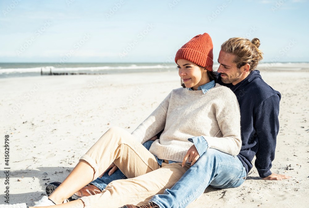 Young couple sitting together on beach sand Young couple sitting together on beach sand