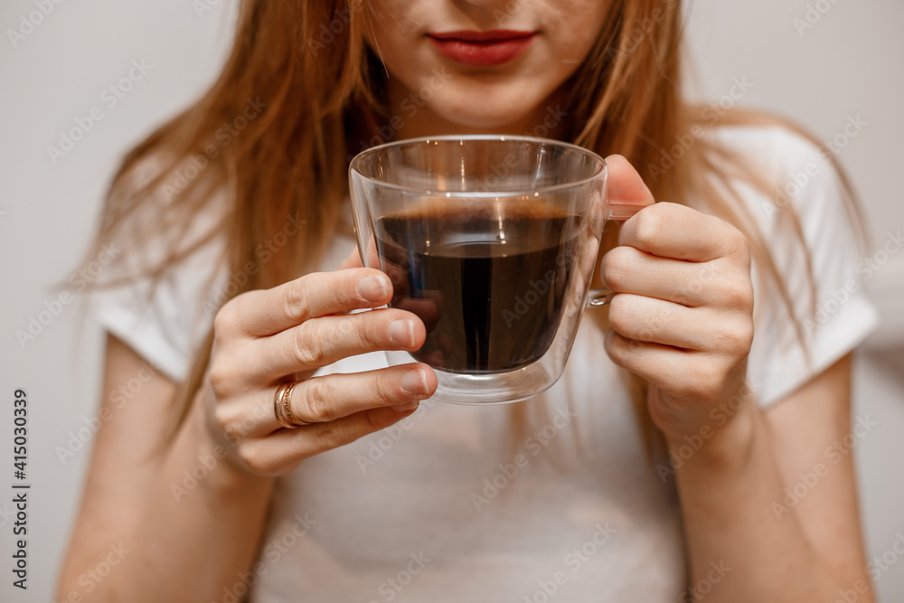 Woman hands holding mug of hot drink. She is smiling and holding a cup of coffee in hand split up in order to inhale the aroma of coffee. Beautiful Girl Drinking Coffee in home. Woman hands holding mug of hot drink. She is smiling and holding a cup of coffee in hand split up in order to inhale the aroma of coffee. Beautiful Girl Drinking Coffee in home.