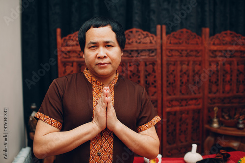 Thai man smiling portrait with traditional Thai suit and welcome pray gesture folded hands photo