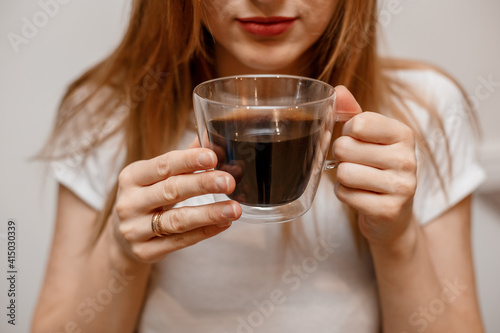 Woman hands holding mug of hot drink. She is smiling and holding a cup of coffee in hand split up in order to inhale the aroma of coffee. Beautiful Girl Drinking Coffee in home.