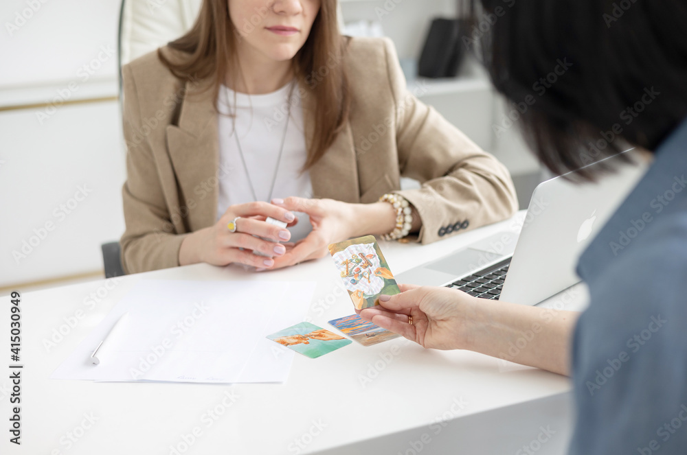 two young women conduct a coaching session in home office in light interior with laptop and flowers on tablework with metaphorical cards and psychological counseling two young women conduct a coaching session in home office in light interior with laptop and flowers on tablework with metaphorical cards and psychological counseling